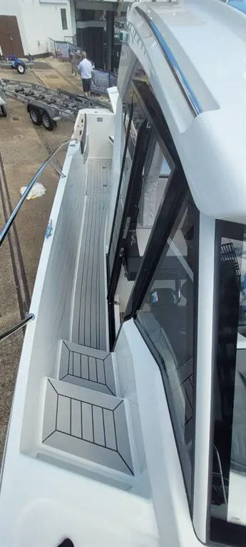 Modern boat interior showing sleek design, steps, and a person in the background by the dock. Boat features gray flooring.